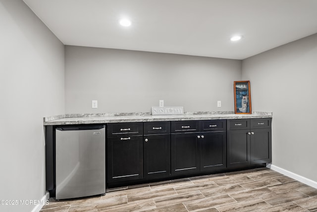 kitchen with light stone counters, dark cabinets, wood finish floors, baseboards, and freestanding refrigerator