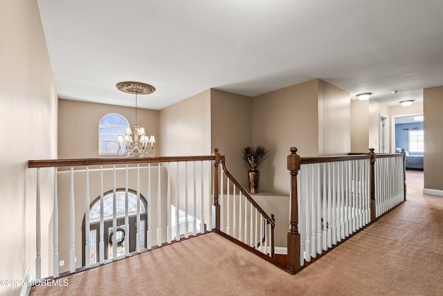 hallway with a chandelier, carpet, baseboards, and an upstairs landing