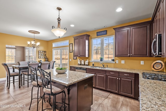 kitchen featuring light stone counters, a kitchen island, a sink, hanging light fixtures, and appliances with stainless steel finishes