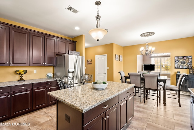 kitchen with stainless steel fridge, visible vents, light stone counters, a center island, and decorative light fixtures