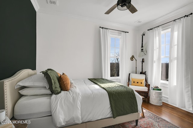 bedroom with ornamental molding, wood finished floors, visible vents, and a ceiling fan