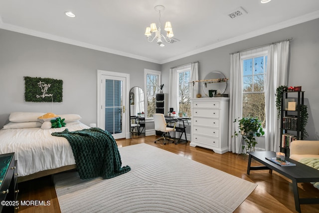 bedroom with a notable chandelier, wood finished floors, visible vents, and crown molding