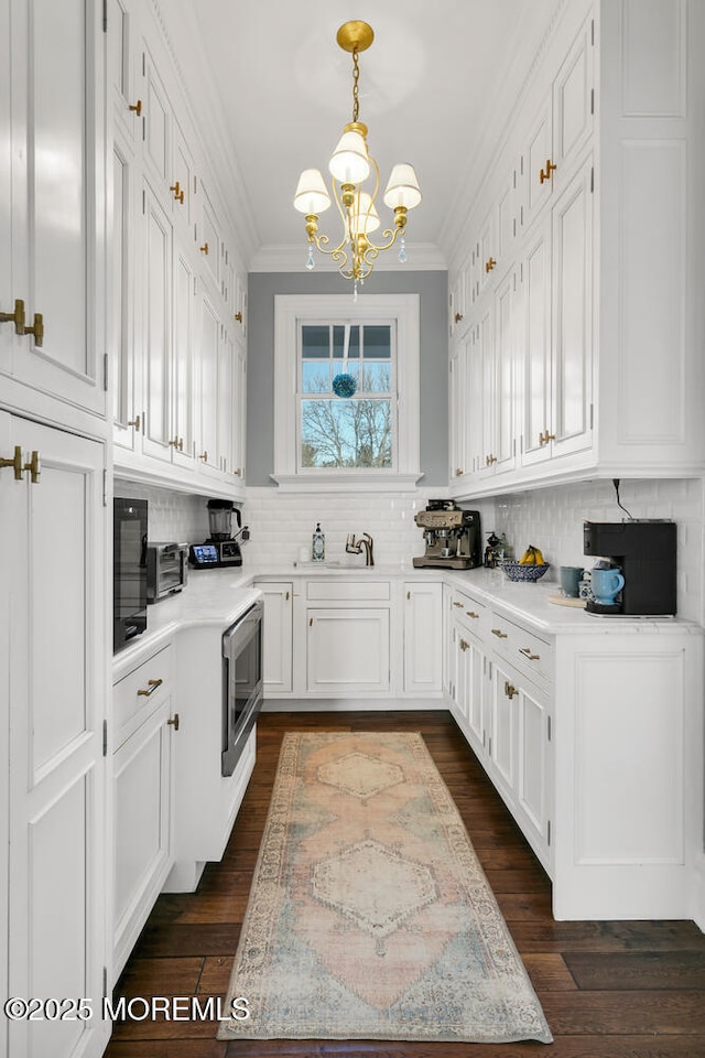 kitchen featuring white cabinets, light countertops, backsplash, stainless steel microwave, and crown molding