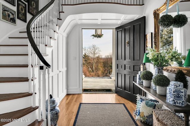 foyer entrance with coffered ceiling, beamed ceiling, stairway, and wood finished floors