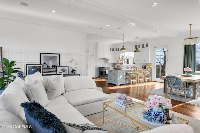 living area with wainscoting, wood finished floors, crown molding, a decorative wall, and recessed lighting