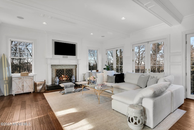 living room with plenty of natural light, dark wood-style floors, ornamental molding, beamed ceiling, and a lit fireplace