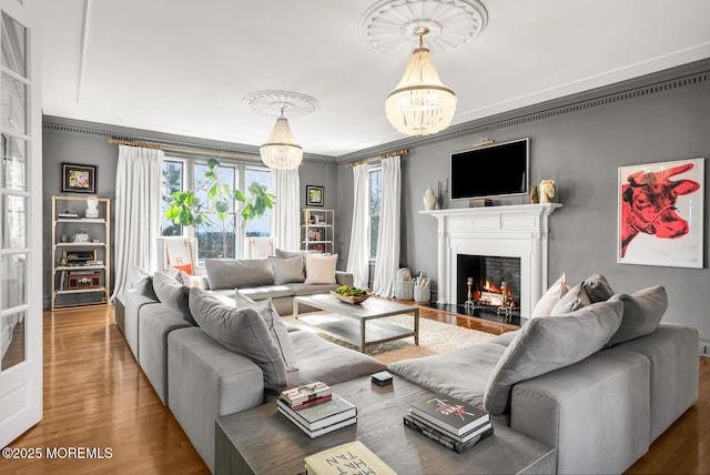 living area with an inviting chandelier, a fireplace with flush hearth, ornamental molding, and wood finished floors