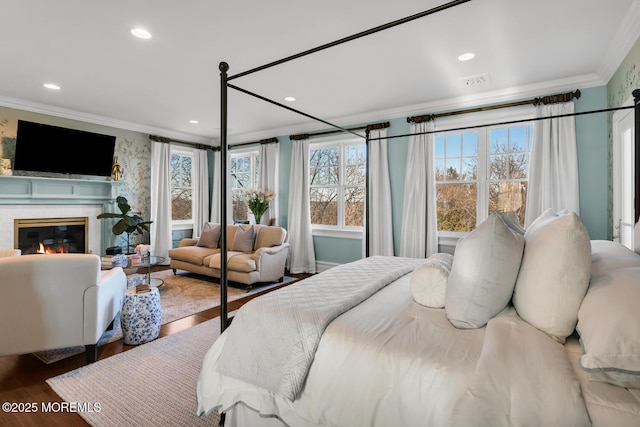 bedroom featuring recessed lighting, wood finished floors, visible vents, ornamental molding, and a glass covered fireplace