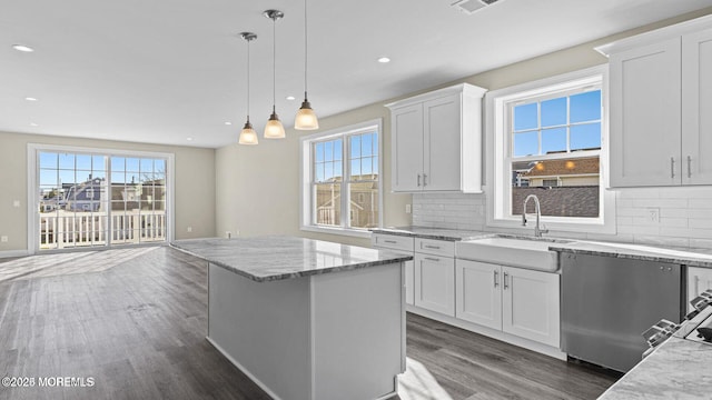 kitchen with white cabinets, a center island, hanging light fixtures, light stone countertops, and a sink