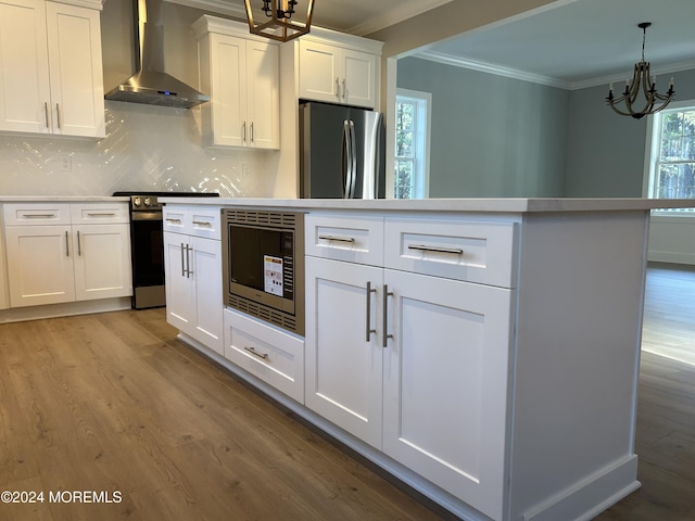 kitchen featuring stainless steel appliances, white cabinets, ornamental molding, light wood-type flooring, and wall chimney exhaust hood