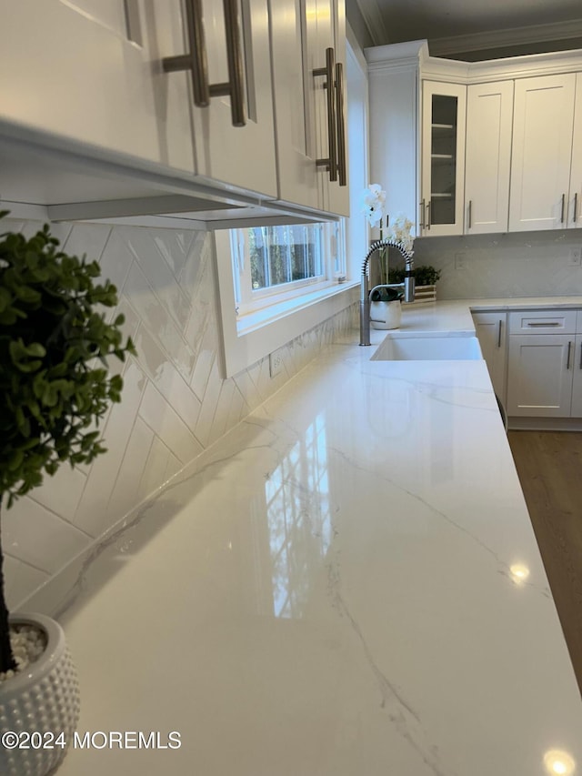 kitchen with light stone countertops, a sink, glass insert cabinets, and white cabinets