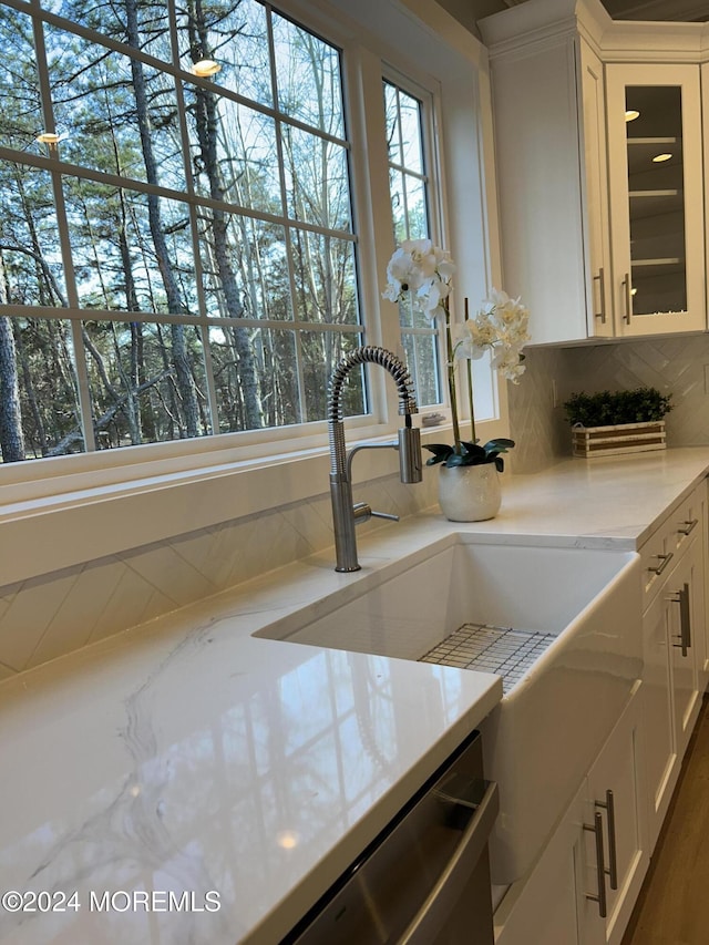 interior details featuring a sink, white cabinets, stainless steel dishwasher, tasteful backsplash, and glass insert cabinets