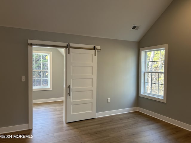 empty room featuring visible vents, a barn door, wood finished floors, and a wealth of natural light