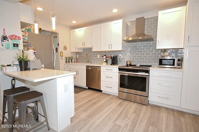 kitchen with appliances with stainless steel finishes, light countertops, white cabinetry, and wall chimney exhaust hood