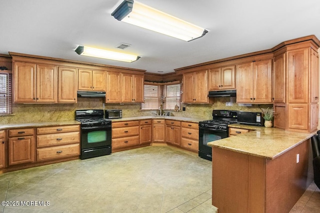 kitchen with a peninsula, black appliances, under cabinet range hood, and visible vents
