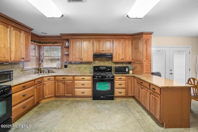 kitchen with light stone counters, a sink, a peninsula, black appliances, and extractor fan