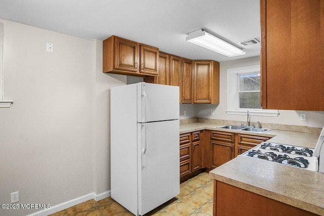kitchen with visible vents, brown cabinets, freestanding refrigerator, light countertops, and a sink