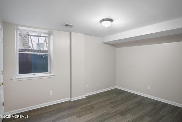 empty room featuring dark wood-type flooring, visible vents, and baseboards