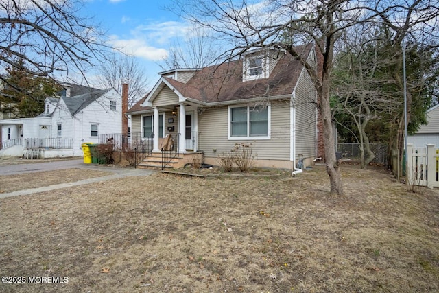 view of front of house with a shingled roof, a chimney, fence, and a porch