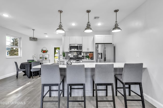 kitchen with light wood finished floors, baseboards, visible vents, stainless steel appliances, and a kitchen bar