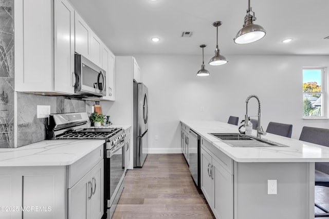 kitchen with visible vents, decorative backsplash, a peninsula, stainless steel appliances, and a sink