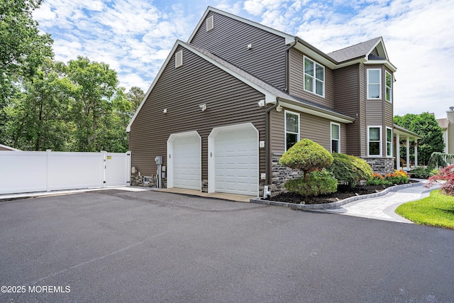 view of home's exterior featuring a garage, stone siding, fence, and driveway