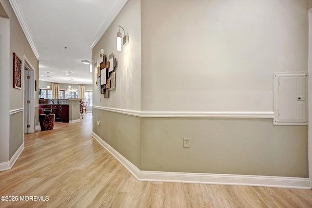 corridor with ornamental molding, light wood-type flooring, electric panel, and baseboards