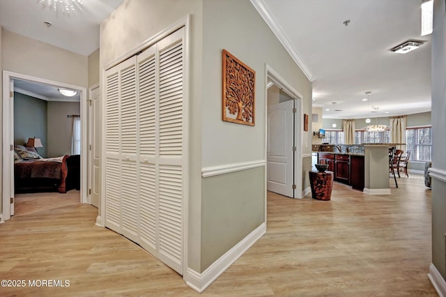 hall featuring light wood finished floors, visible vents, baseboards, and crown molding