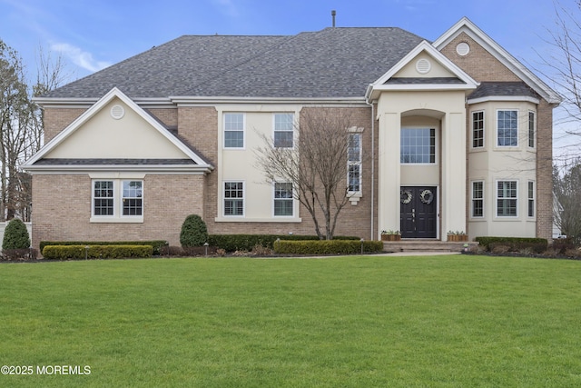 view of front of house featuring a shingled roof, a front lawn, and brick siding