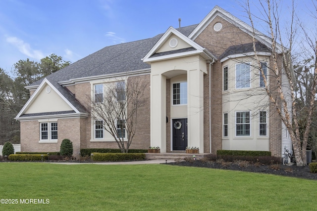 view of front of home featuring brick siding, roof with shingles, and a front yard