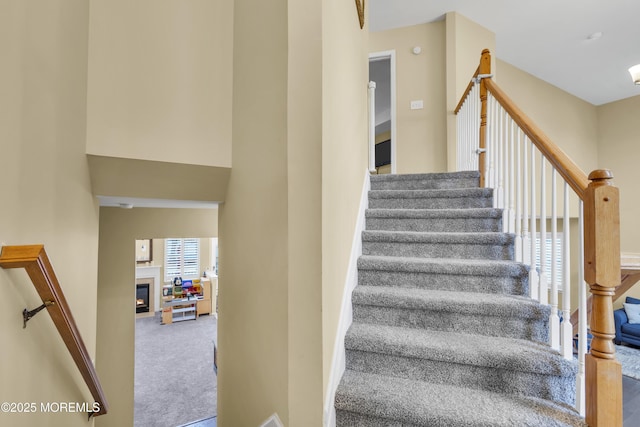 stairs featuring carpet and a glass covered fireplace