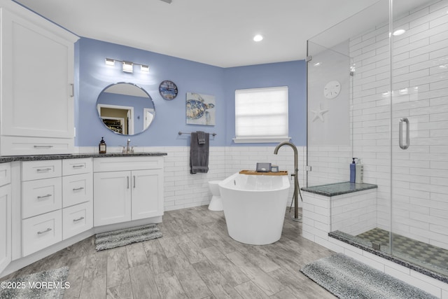 full bathroom featuring a wainscoted wall, tile walls, a soaking tub, a shower stall, and vanity