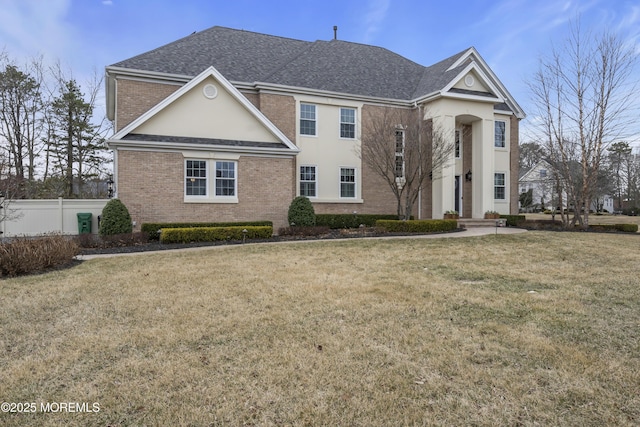 greek revival house with brick siding, stucco siding, a shingled roof, a front yard, and fence