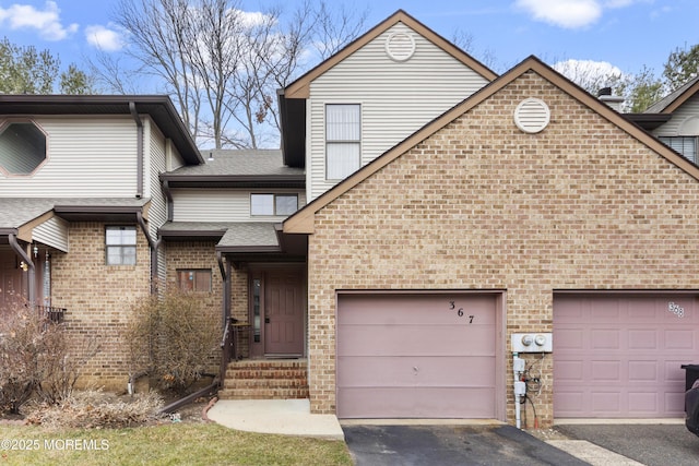 multi unit property with a shingled roof, brick siding, driveway, and an attached garage