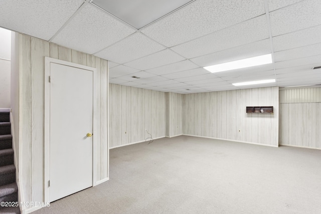 finished below grade area with carpet floors, a paneled ceiling, and stairs