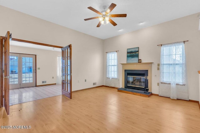 unfurnished living room featuring wood finished floors, a ceiling fan, baseboards, french doors, and a glass covered fireplace