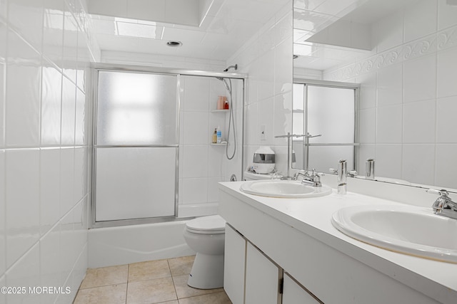 bathroom featuring combined bath / shower with glass door, a sink, tile walls, and toilet