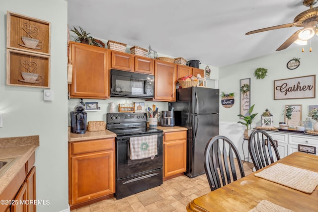 kitchen with a ceiling fan, stone finish floor, brown cabinets, light countertops, and black appliances