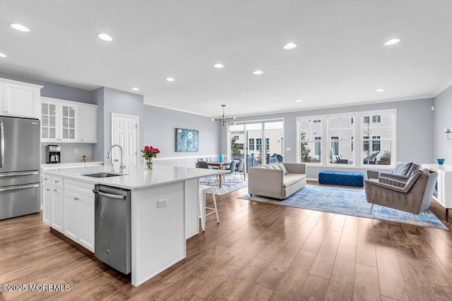 kitchen featuring wood finished floors, a sink, open floor plan, appliances with stainless steel finishes, and glass insert cabinets