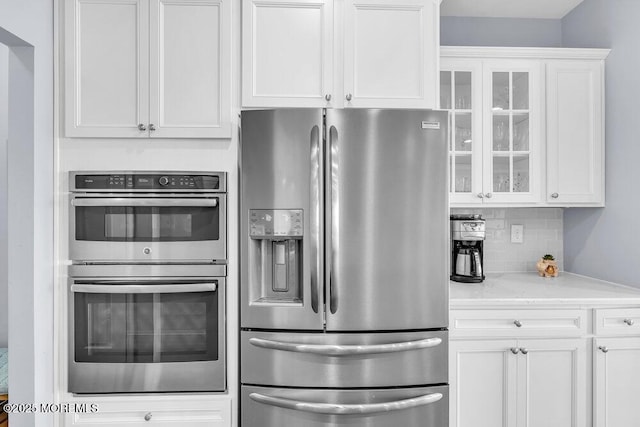 kitchen featuring white cabinets, glass insert cabinets, stainless steel appliances, and backsplash