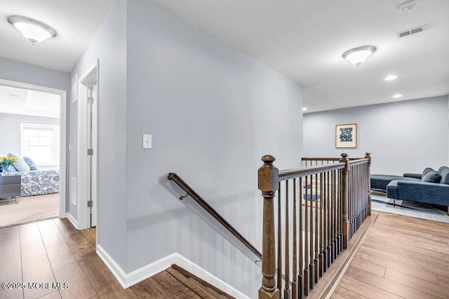 hall featuring baseboards, visible vents, an upstairs landing, and wood finished floors