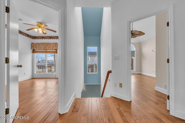 corridor featuring light wood-style floors, visible vents, baseboards, and an upstairs landing