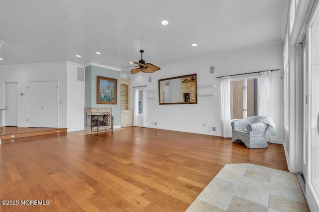 living room with ceiling fan, ornamental molding, a fireplace, and wood-type flooring