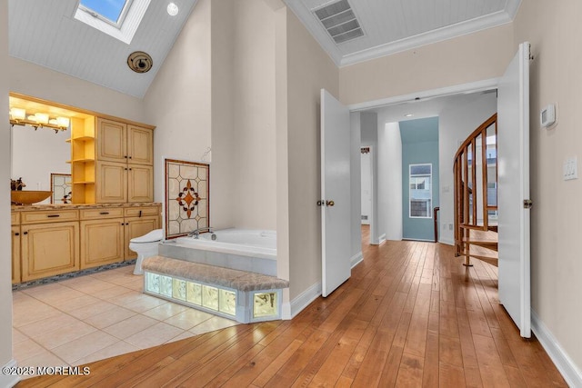 hall with high vaulted ceiling, a skylight, visible vents, stairway, and light wood-type flooring