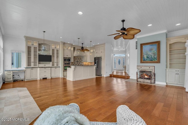 living area with a lit fireplace, light wood-style floors, recessed lighting, and crown molding