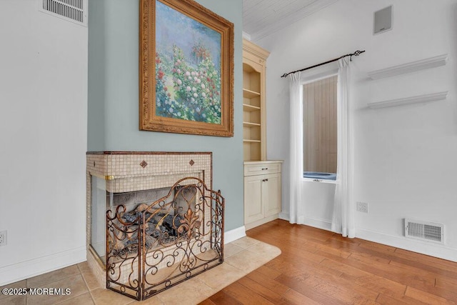 interior space featuring baseboards, a fireplace, visible vents, and wood finished floors