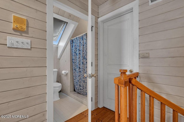 full bath featuring a skylight, a shower with curtain, wooden walls, and toilet