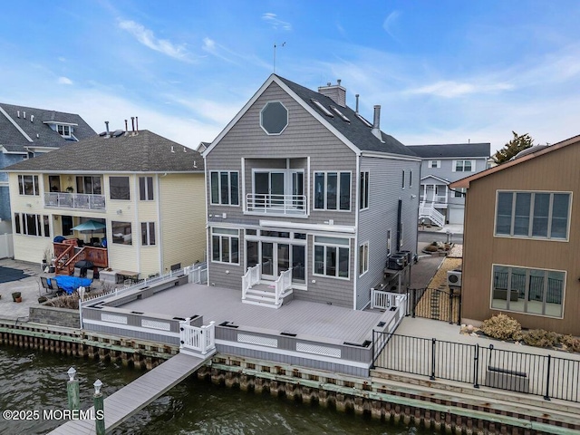 back of house featuring a balcony, a deck with water view, fence, a gate, and a chimney