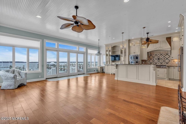 unfurnished living room featuring light wood-type flooring, ornamental molding, and a ceiling fan