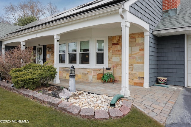 property entrance featuring a shingled roof, stone siding, covered porch, and roof mounted solar panels